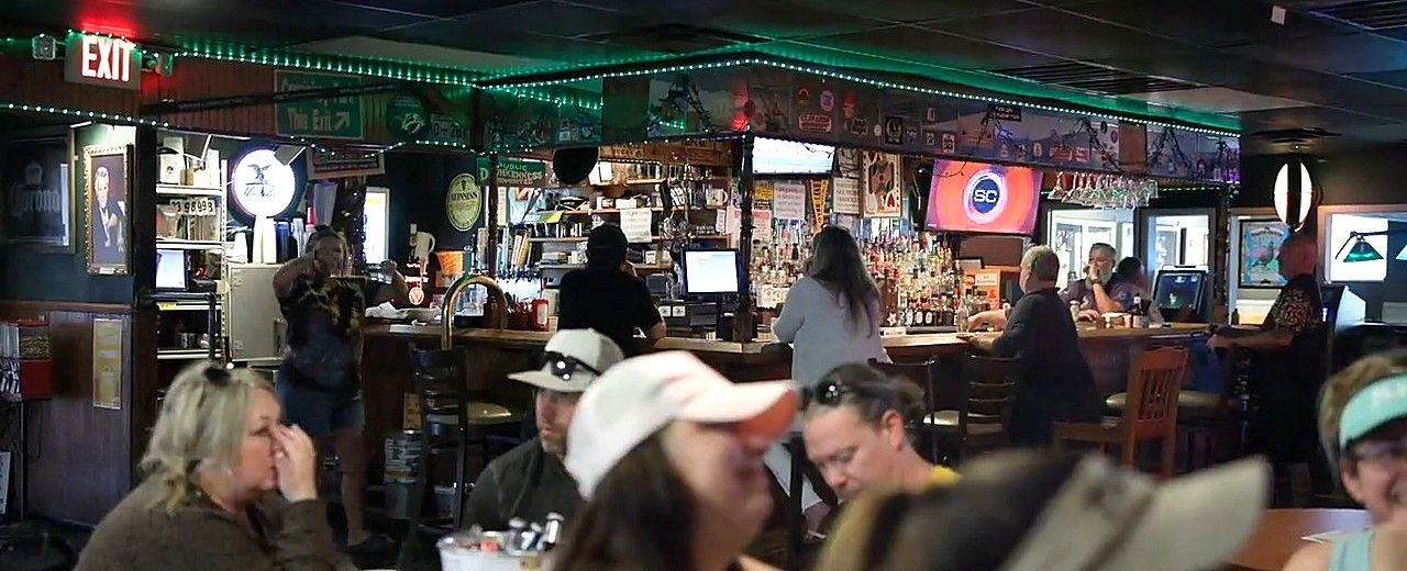 The bar at Bar South on a busy night: regulars on the stools, the back bar lit, the game on